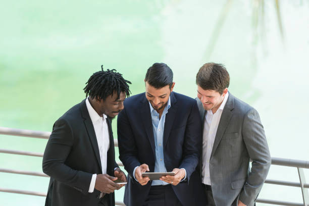 Three businessmen review documents on a tablet, discussing Ajman Free Zone license costs.